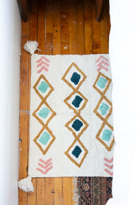 Small accent rug with pink, teal and mustard designs and pom poms 